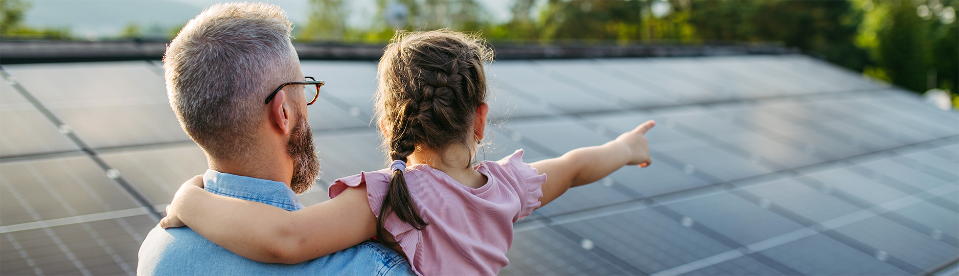 Father holding daughter next to solar panels